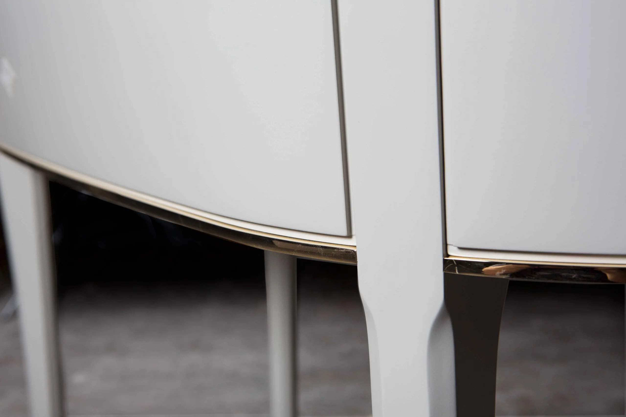 Close-up of a white cabinet with a curved design and gold trim detailing at the base.