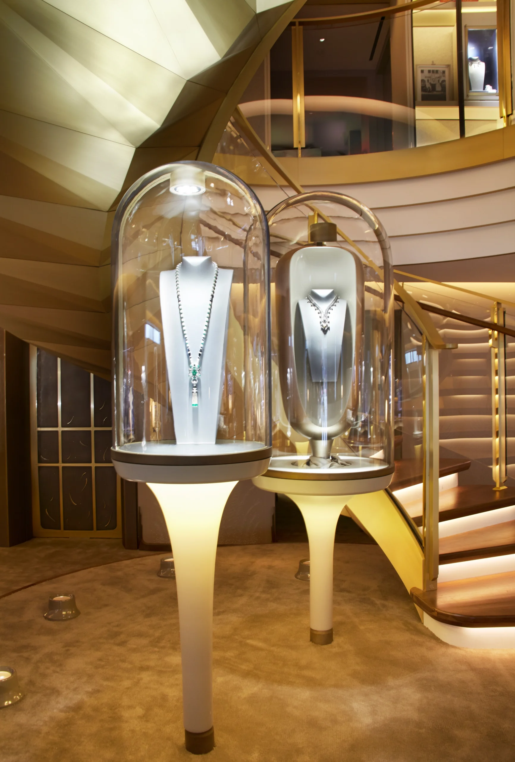 Luxury necklaces displayed under glass domes in a posh interior with spiral staircases.